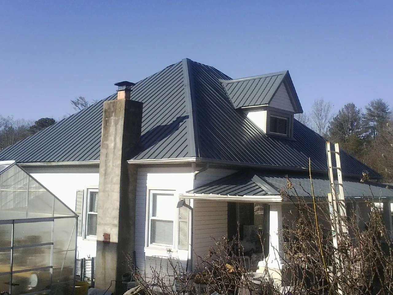 Dark blue standing seam metal roof on a white farmhouse with dormer — Slate & Tile Roof Repair by Roofing Brothers in Mazomanie