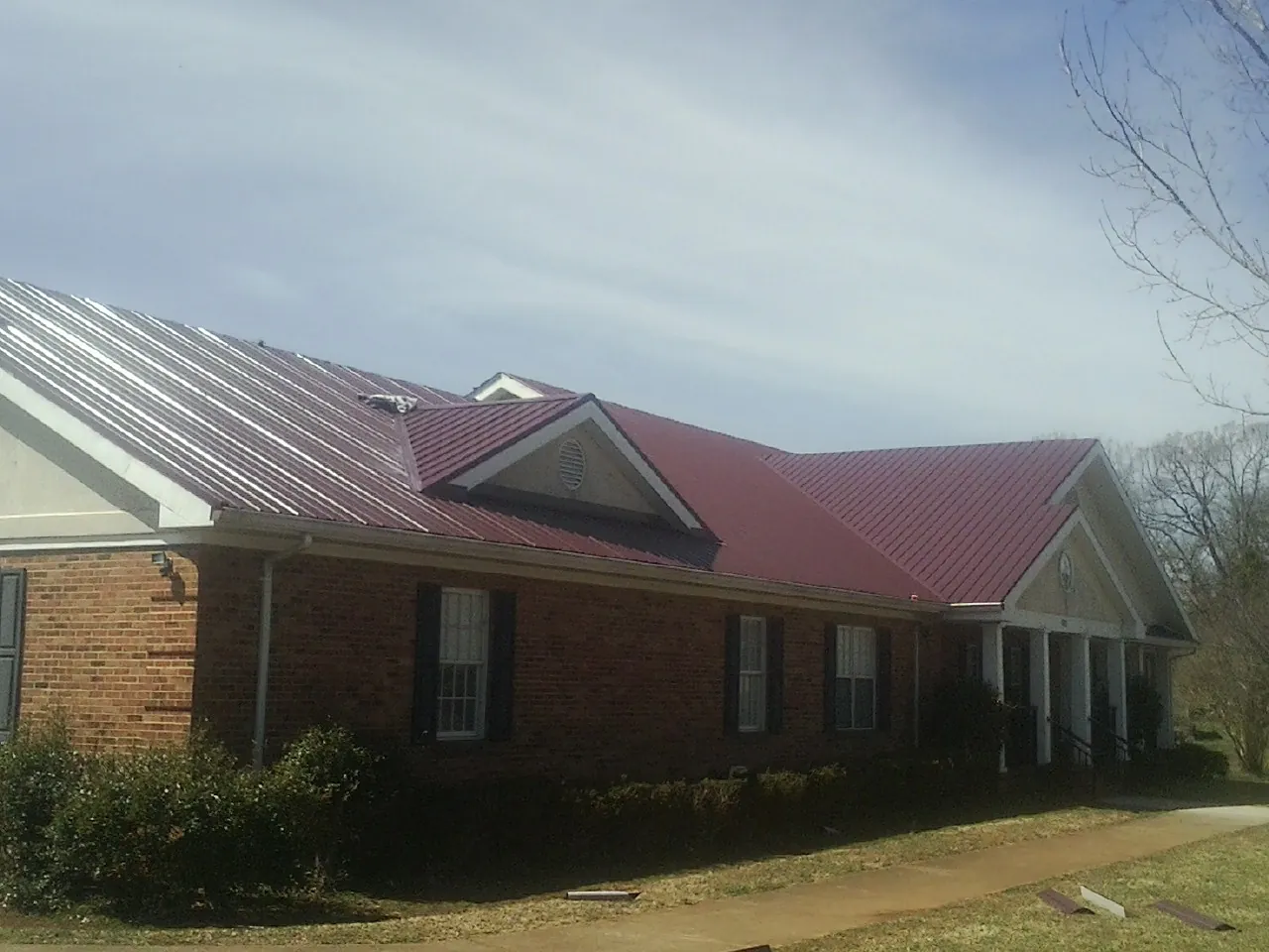 Red metal roof with gabled entries on a long brick building, from a Hail Damage Roof Repair job in Mazomanie