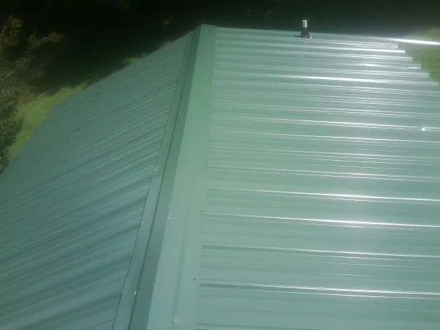 New green metal panels meeting at the ridge of a roof — Flat Roof Repair work by our crew in Mazomanie