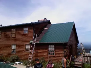 Green metal roof going on a two story log home with ladders set in Mazomanie