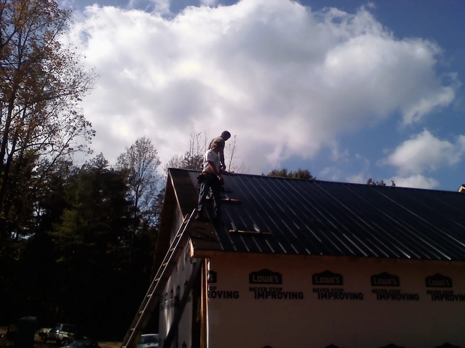 Roofer fastening dark metal panels high against a cloudy sky, from a Roof Inspection job in Mazomanie