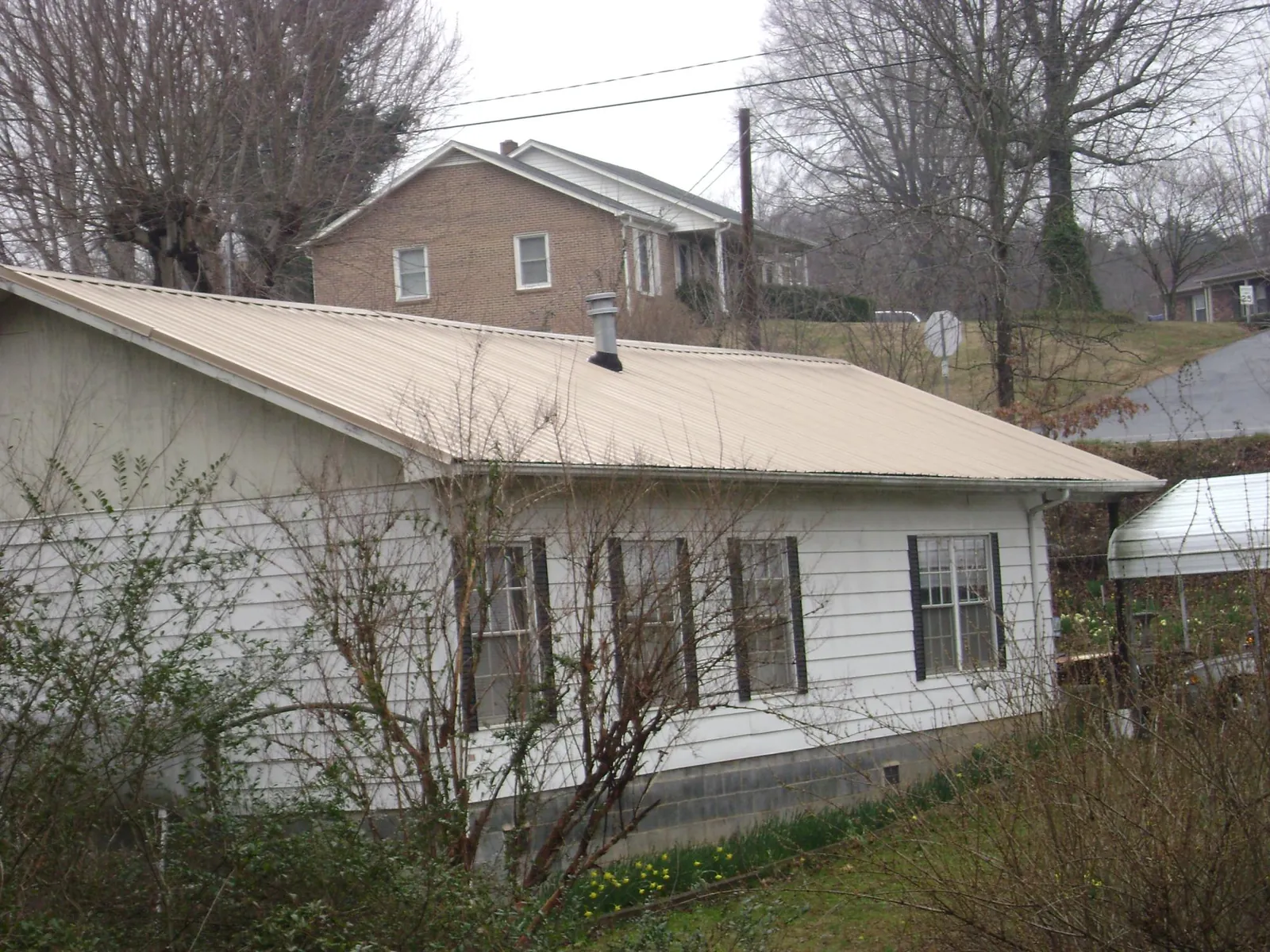 Tan metal roof on a white sided house set into a hillside — Commercial Roofing by Roofing Brothers in Mazomanie